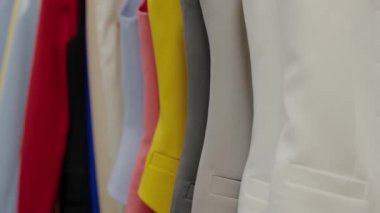 Kıyafet rafında düzgün bir şekilde asılı duran canlı ceketlerden oluşan bir koleksiyon. Tarz, moda ve perakende alışverişini temsil ediyor. Renkli Blazer 'lar Moda Mağazasında Bir Rafta Asılı