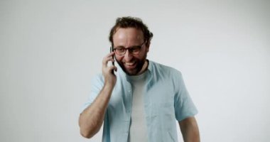 Telefonda konuşan mutlu adam. Açık mavi bir gömlek ve gözlük takıyor. Hattın diğer ucundaki kişiyi dinlerken gülüyor ve gülümsüyor. Arka plan basit ve parlak beyaz.