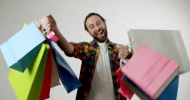 Alışveriş torbalarıyla heyecanlı bir adam. Mutlu müşteri alışverişini, mevsimlik satışını, alışveriş çılgınlığını seviyor. Beyaz arka planlı stüdyo çekimi. Düşük açı görünümü.