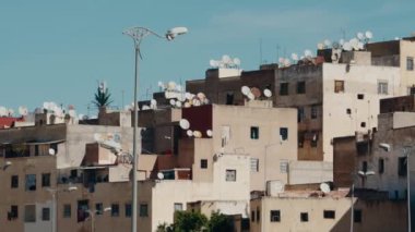 Uydu antenleri Fas 'ın bir şehrinin çatılarını dolduruyor, geleneksel mimari ve modern teknolojinin bir karışımını yakalıyor. Açık mavi gökyüzünün altında,