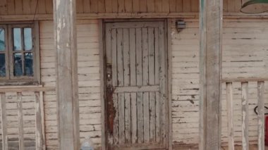 Eski, yıpranmış ahşap kapı ve Fas 'ta terk edilmiş bir evin verandası. Boya soymak ve kırık camlar kırsal çekiciliğe katkı sağlıyor. Bu sahne nostalji, tarih ve çürümeyi çağrıştırıyor..