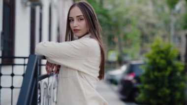 Açık havada sakin bir şehir arkaplanıyla duran kendinden emin genç bir kadının portresi. Sakinlik ve özgüven yayıyor. Kentsel Çevre 'de Kendine Güvenen Genç Kadın Poz Veriyor