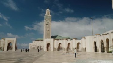 Hassan II Camii, Kazablanka, Fas 'ta. Büyük beyaz cami önünde büyük bir meydanda yürüyen insanların geniş bir görüntüsü. Mavi gökyüzü ve beyaz bulutlarla güneşli güzel bir gün..