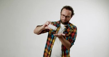 Sakallı ve gözlüklü bir adam eline beyaz bir şişeden ilaç döküyor. Tereddüt ediyor ve emin değil. Bu video ilaç, tedavi ve sağlık konularındaki belirsizliği yansıtıyor.