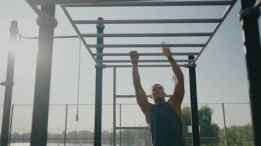 Atletik bir adam, açık hava fitness parkındaki demirlerde barfiks çekiyor. Güneş arka planda hafifçe parlıyor, canlı ve motive edici bir atmosfer yaratıyor. Odaklanmış Sporcu
