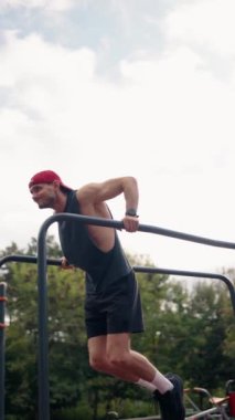 Kararlı bir erkek sporcu, açık hava parkı ortamında paralel barlara daldı. Spor konsepti videosundaki antrenmanına odaklanıyor. Spor, spor, motivasyon ve atletizm için ideal.