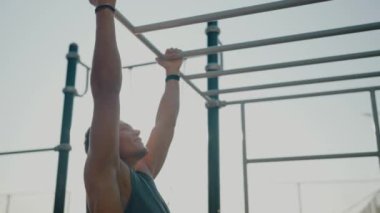 Açık hava fitness parkında çalışan formda bir genç adam açık havada azim ve fiziksel güç sergiliyor. Genç Adam Spor Salonu 'nda Maymun Barları Üzerinde Egzersiz Yapıyor