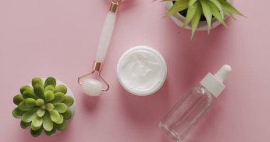Üst görünüm beyaz şişe, serum, yüz pembesi silindiri stüdyoda pembe arka planda kozmetik için dönüyor. Doğal malzemelere dayalı kozmetik yağı, fırça, tonik, vücut bakımı. Kavanoz kremi, yüz silindiri, serum.