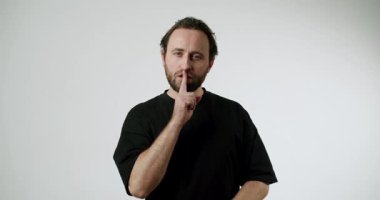 Siyah tişörtlü adam parmaklarını dudaklarına dayayıp sessizlik istiyor. Vücut dili. - Gizli. Gri arka plan. Orta boy. Sessizlik, Vücut Dili, Gizli İsteyen Adam,