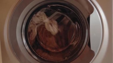 Çamaşır makinesinde dönen kıyafetler. Çamaşır günü, ev işleri ve temizlik. Kıyafetler sabun ve suyla yıkanıyor. Çamaşır makinesi en iyi silahtır..