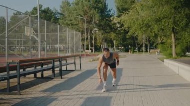 Atletik giyinen genç bir adam açık güneşli bir günde kaldırımda koşuyor. Vücut geliştirme, kararlılık ve açık hava aktivitesi. Genç bir adam güneşli bir günde parkta koşuyor.