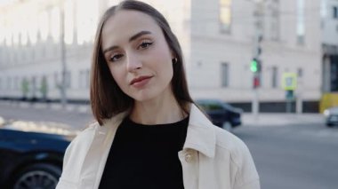 Kendine güvenen genç bir kadın gün boyunca işlek bir şehir caddesinde sakin ve kendinden emin bir şekilde duruyor. Duygulara ve modaya odaklı şehir portresi. Şehir Caddesinde Kendine Güvenen Kadın