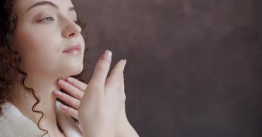 Yüzü sağlıklı cilt masajı elleriyle beyaz bornozlu güzel kadın yüzüne dokunuyor. Yüzüne nazikçe dokunup okşayan beyaz bornozlu genç bir kadın..