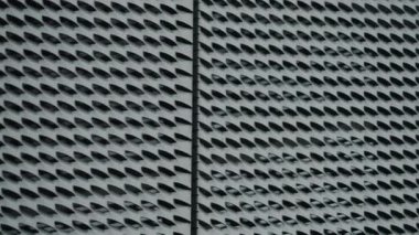 Tekrarlanan geometrik metal ekran desenli modern binaların ön cephelerine yakın çekim. Gri metalik doku, ışık ve gölge etkileşimi ile soyut bir tasarım yaratır. Mimarlık için ideal