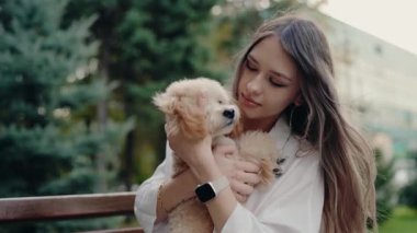 Genç bir kadın sevimli tüylü köpeğini parkta nazikçe tutuyor. Güneşli bir günde tüylü arkadaşını sevgiyle okşar. Aralarında özel bir bağ var. Beyaz gömleği köpek kürkünü tamamlıyor..