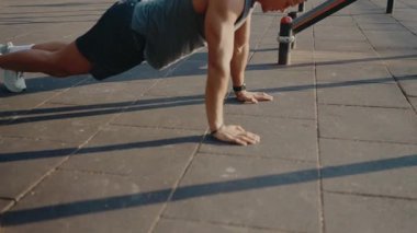 Açık şehir parkında şınav çeken fit bir adam. Dayanıklılık, zindelik ve egzersiz konularına kararlılık temalı odaklan. Şehir Spor Parkı Ayarları 'nda şınav çeken adam.