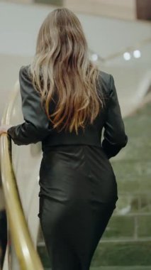 Siyah takım elbiseli, güneş gözlüklü, şık ve modern bir iç mekanda akıllı telefon tutan kendine güvenen bir kadın. Moda, güven ve iş konuları için ideal. Modaya uygun genç ve güzel bir kadın. Dikey.