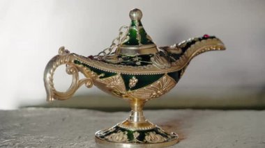 Süslü altın ve yeşil sihirli lamba. Bu cin lambası bir taşın üzerinde duruyor. Bir dilek tut. Fantezi, peri masalı ya da Arap Geceleri teması için harika. Bu büyülü nesne dilekleri, hayalleri ve iyi kaderi temsil ediyor..