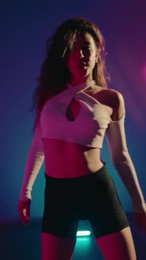Genç bir kadın neon ışıkları değişen renkli bir stüdyoda dans ediyor. Kendine güveni ve enerjisiyle hareket ediyor, dansa olan tutkusunu gösteriyor. Genç Kadın Neon Lit Stüdyosunda Şehvetle Dans Ediyor