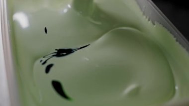 Yeşil jelatin tatlısının sanatsal yakın çekimi. Açık bir kapta koyu siyah mürekkep kıvrımlı. Yeşil jel tatlısına yakın plan Siyah Mürekkep Tasarımı