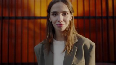 Genç profesyonel bir kadın canlı turuncu bir şehir arka planının önünde poz veriyor. Düşünceli ifadesi güven ve zarafeti çağrıştırıyor. Güzel, kendine güvenen kadın kamerada poz veriyor.