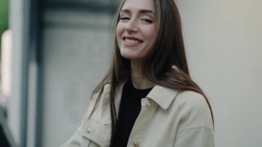 Uzun saçlı genç bir kadın açık havada sıradan bir ceketle dikilirken sıcak bir şekilde gülümsüyor. Onun mutlu tavrı parlak bir günün doğal ışığıyla vurgulanır. Sıradan ceketli, gülen kadın.