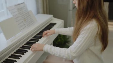 Genç kız evde piyano çalışıyor. Eğitim ve öğrenim geliştirme konsepti. Odaklanmış genç, güzel bir kız. Elektrikli piyano çalarak eğleniyor. Nota okuyorum. Piyano öğrenme dersleri
