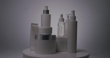 Beyaz şişeler ve tüpler, stüdyoda beyaz arka planda kozmetik için dönen serum, karanlıktan gelen ürünlerde ışık görünür ve parlar. Doğal malzemelere dayalı kozmetik yağları, fırça, tonik.
