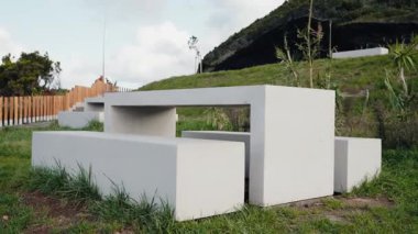 Çimlerin, tepelerin ve çitlerin yemyeşil olduğu manzaralı bir açık havada modern beton piknik masası. Açık hava aktiviteleri, rahatlama ve doğanın tadını çıkarmak için idealdir. Somut Piknik Tablosu