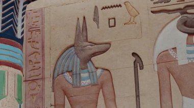 Anubis 'i tasvir eden Antik Mısır duvar kabartması, ölüler tanrısı. Karmaşık sanat eserlerinde canlı renkler ve detaylı hiyeroglifler, zengin tarih ve antik Mısır mitolojisi sergileniyor..