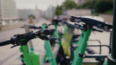 Portekiz 'de bir şehir caddesinde arka arkaya park etmiş yeşil elektrikli scooterların yakın çekimi, kentsel hareketlilik ve çevre dostu ulaşımı vurguluyor. Kentsel Ayarlara Park Edilmiş Elektrikli Scooter Sırası