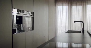 Pürüzsüz ve şık bir modern mutfak. İçinde üst düzey aletler, minimalist dolaplar ve geniş bir tezgah var. Dahili Aletler ve Minimalist Tasarımlı Modern Mutfak