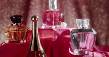 İncili pembe kumaş ve parıldayan bokeh arkaplan üzerinde çeşitli şekillerde sergilenen zarif parfüm şişeleri koleksiyonu. Güzellik, moda ve lüks kavramlar için mükemmel..