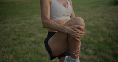 Genç atletik kadın antrenmandan önce ısınıyor. Sportif kadın üstte ve şortlar parkta fiziksel egzersizden sonra taş üstüne bacak esnetiyor. Sıhhat etkisi arttırıcı ısınıyor. Dişi esneme bacakları.