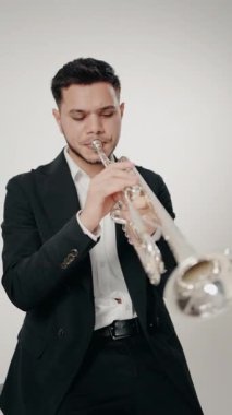 Modern bir stüdyoda beyaz arka planda trompet çalan bir erkek caz şarkıcısı. Canlı caz konseri. Müzik tutkusu. Genç trompetçinin yakın eli. Müzik odası. dikey video.