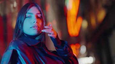 Işıkların arkasında kameraya poz veren güzel bir kadın. Lüks kadın portresi. Neon ışıkları. Model pozu şehir caddesi. Geceleri şehir merkezinde poz veren güzel bir kadın..