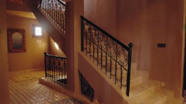 Süslü demiri olan zarif Fas merdiveni. Ilık ışık filtreleri, sakin bir ortam yaratıyor. Bu karşılama alanı geleneksel tasarım modern konforun büyüleyici bir karışımını sunuyor.