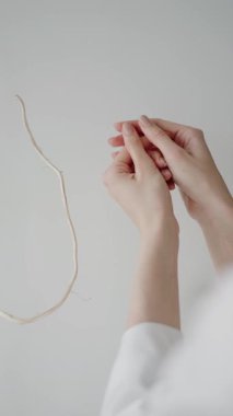 Minimalist ve yumuşak bir arkaplana karşı ince bir dalı nazikçe tutan ellerin yakın plan görüntüsü. Fotoğraf, narin detayların güzelliğini vurgulayan bir sakinlik ve sadelik hissi yayıyor..