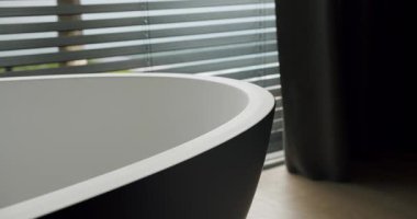 Lüks bir banyoda, modern, oval, serbest banyo küvetine yakından bak. Panjurların arasından süzülen, zarif, minimalist bir tasarım sergiliyor. Modern Serbest Yüzme Küveti