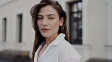 Kendine güvenen genç bir kadının portresi. Zarif bir gülümsemesi var. Şık beyaz bir gömlek giyiyor. Şık Beyaz Gömlekli Kendine Güvenen Genç Kadın Şehir Ayarları 'nda