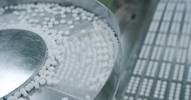 İlaç fabrikasının atölyesinde metal otomatikler üzerinde hareket eden beyaz haplar. Hap ve uyuşturucu üretimi süreci. Fabrika ekipmanı ve makine. Uyuşturucuya yakın görünüm taşıyıcı bant boyunca ilerler.