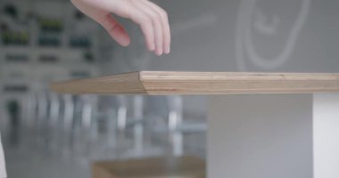 Modern olarak tasarlanmış bir kafe ortamında, insan elinin zarif, ahşap bir masanın yüzeyine nazikçe dokunuşunun yakın plan görüntüsü. Kentsel bir ortamda huzur ve sadelik anı.