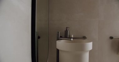 İçinde minimalist bir lavabo olan, sabun makinesi ve büyük bir ayna olan modern bir banyo. Tarafsız tonlar ve parlak tasarım çağdaş ve temiz bir atmosfer yaratıyor. Modern Banyo