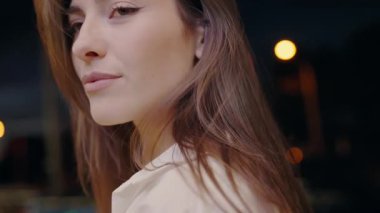 Arkasından geceyi aydınlatan yumuşak odaklı şehir ışıklarıyla zarif genç bir kadının yakın çekimi. Şehir hayatı, güzellik ve tefekkür konuları için mükemmel. Zarif Kadın Portresi