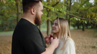 Manzaralı bir sonbahar parkında, birbirlerine nazikçe dokunup bakarken sevgi ve şefkat gösteren genç bir çift arasında romantik ve samimi bir an. Autumn Park 'ta Romantik Çift