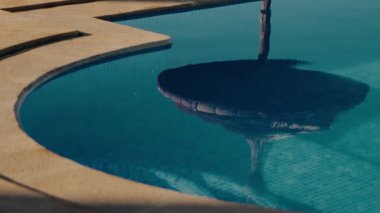 Fas havuzundaki sazdan yapılmış bir şemsiyenin sakin bir yansıması. Turkuaz su şemsiyeyi yansıtır, dingin ve davetkar bir atmosfer yaratır. Seyahat ve turizm için mükemmel.,