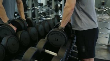 İyi donanımlı bir spor salonunda ağırlık seçen odaklanmış bir adam sağlığa olan bağlılığını vurgular. Egzersiz sırasında Modern Spor Salonu 'nda Dambıl Seçen Adam
