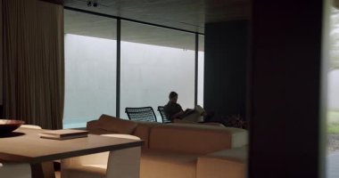 Kanepede dinlenen, modern, minimalist bir oturma odasında kitap okuyan bir adamın huzurlu bir sahnesi. Nötr renk paletiyle sakin ve huzurlu bir ortam. Modern Minimalist Oturma Odasında Rahatlayan Adam