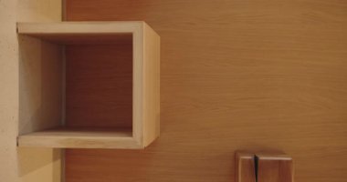 Pürüzsüz, ahşap bir duvara monte edilmiş minimalist ahşap bir rafı gösteren bir resim. Basitlik ve doğal ahşap tanecikleri modern ve temiz bir estetik sağlıyor. Dikey video.