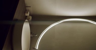 Zarif bir lavabo ve LED ışıklandırmalı yuvarlak bir aynanın olduğu çağdaş bir banyo. Modern iç tasarım ve lüks ev dekorları için mükemmel. Dikey